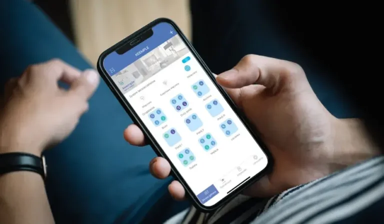 W dłoniach telefon, na ekranie widoczne ikony urządzeń Smart Home Keemple, dom wyposażony w technologie smart home. Aplikacja Keemple 2.0